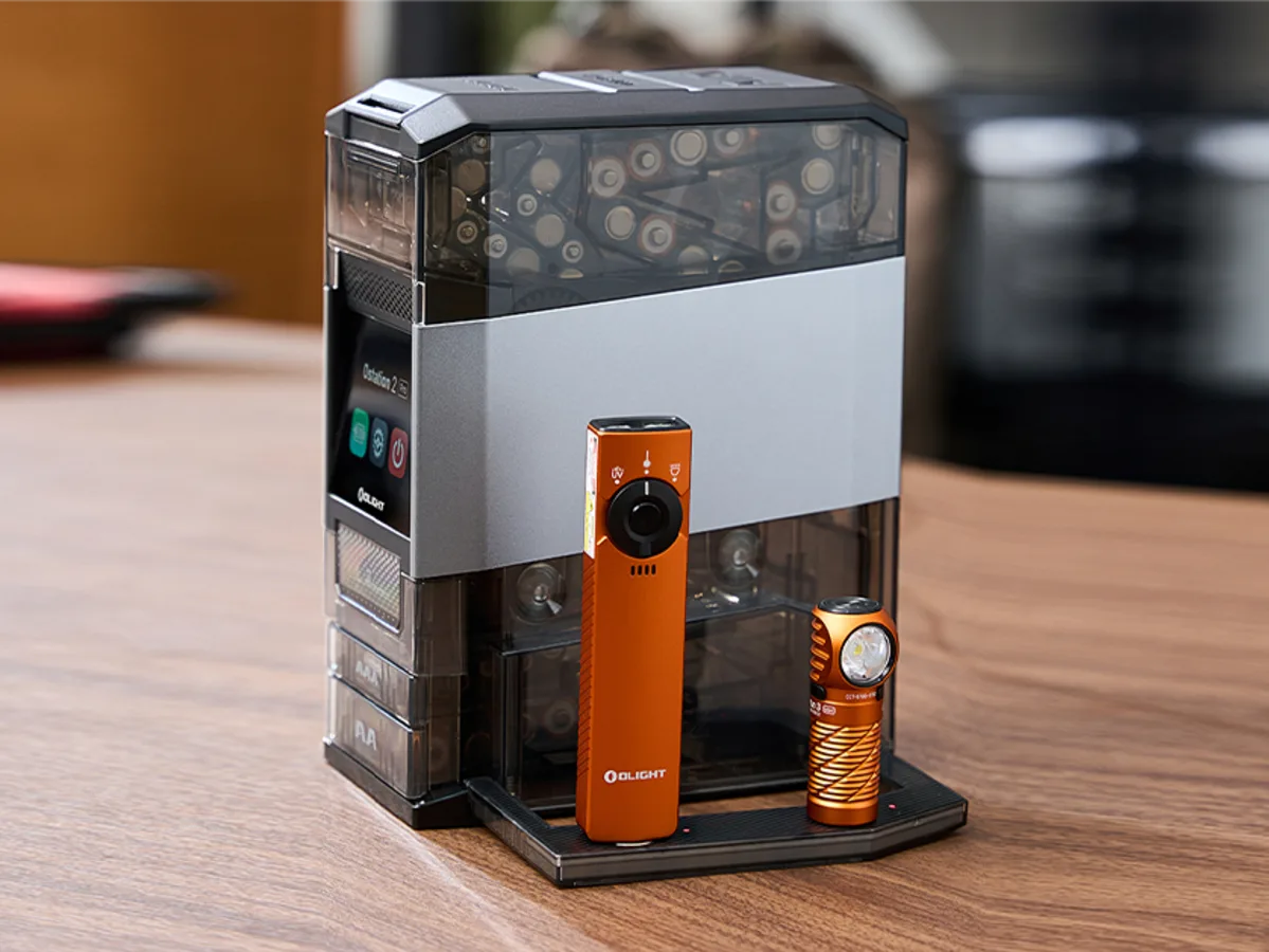 Olight Ostation Smart Battery Care Olight Ostation smart battery station operating beside a desktop monitor