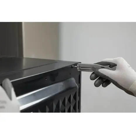 Olight Opry 2 Multi-Tool Pry Bar - gloved hand using grey pry tool against metal fitting Olight Opry 2 Multi-Tool Pry Bar - gloved hand using grey pry tool against metal fitting